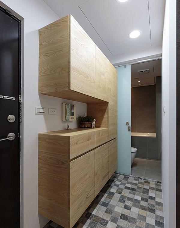 玄关处设计了一个原木的吊柜，方便收纳，透过磁砖拼接、跳色，将收纳柜与卫浴间区域分隔。