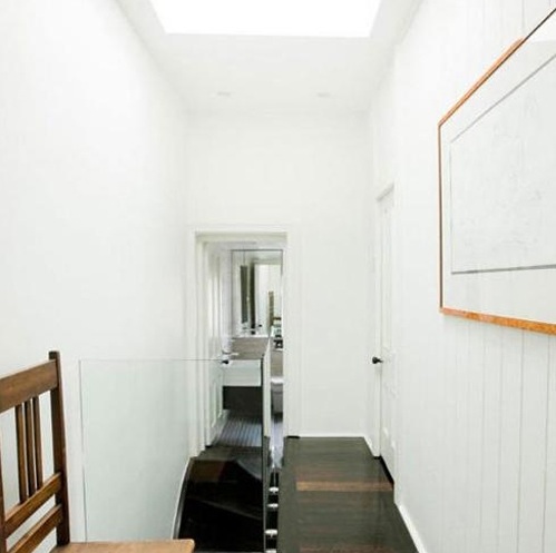 走上楼梯，过道仍然狭窄，设计师在屋顶位置开辟天窗，借助自然光与白色墙面使空间通透。这样美好的光线可不能浪费，放几把简单的椅子，方便阅读哦~