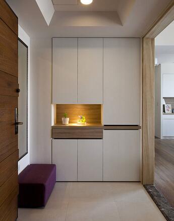 进入屋内，玄关以白色系柜子搭配内嵌橡木台面，地面以不同材质区分客厅与玄关区域。