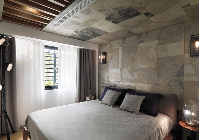 卧室的整体设计上展现了时尚与经典相融合的美感。深浅不一的石板装饰床头墙面，衔接到床尾部分的吊顶则用了木质格栏，通透而精致。