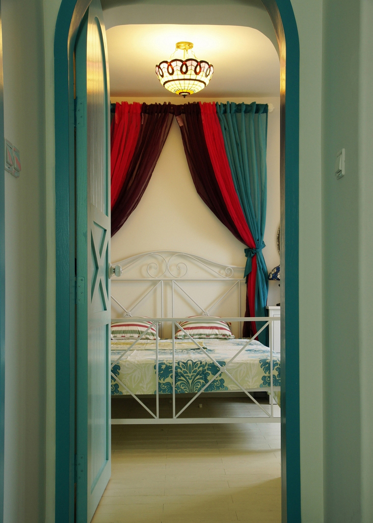 奶绿色的木门打开之后是一个简洁的双人床。床后墙创意地用颜色艳丽的窗帘代替，让整个空间不至于太空白。
