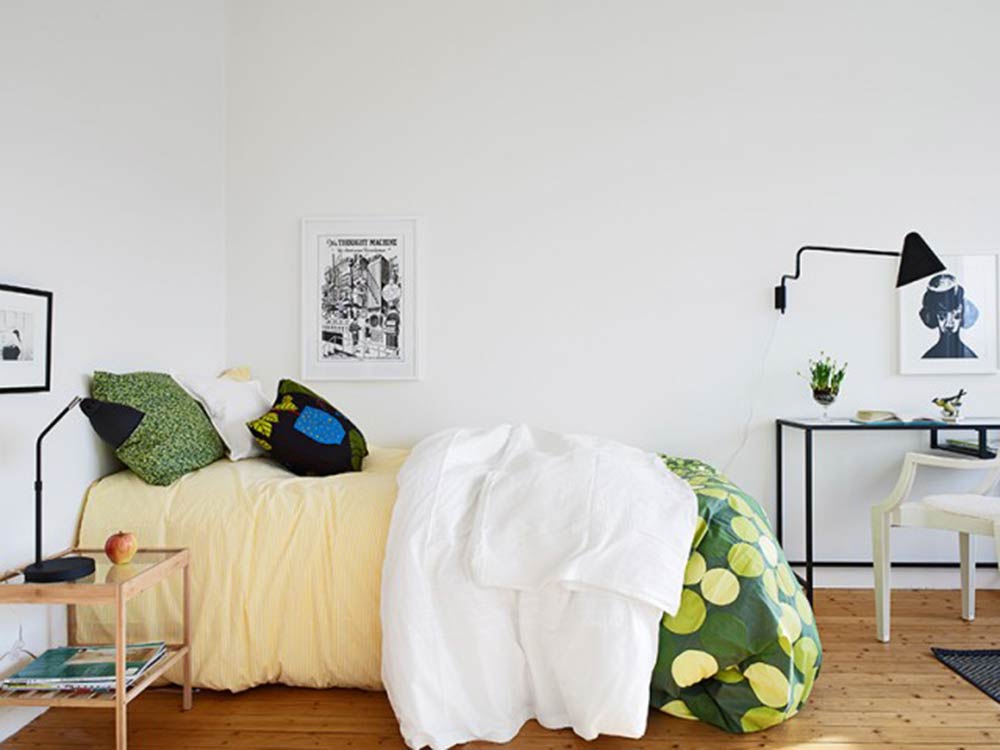 卧室中仍有艺术画装饰，床头的绿色抱枕与绿色被套呼应。床头的桌子与台灯设计简约，线条分明。