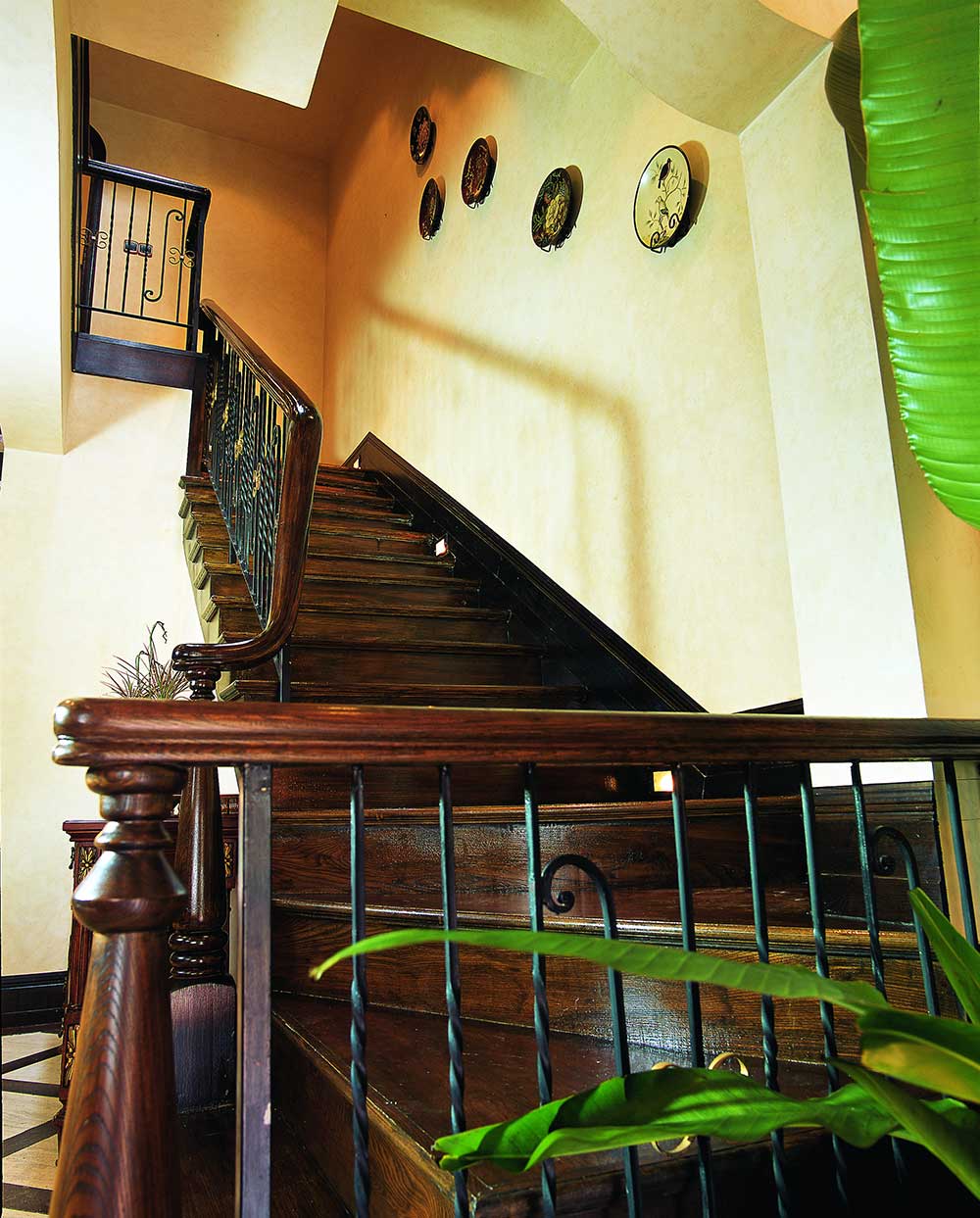 深褐色的楼梯、扶手与浅褐色的壁纸形成对比，并有多个圆盘瓷器装饰，填充了空白。