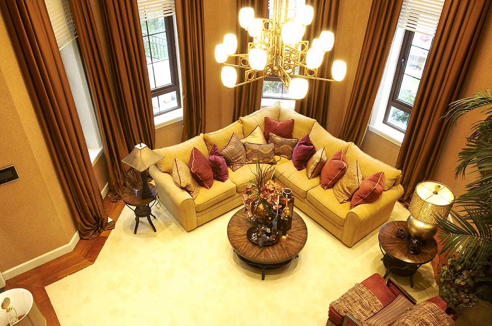 客厅里L型沙发摆放贴合整个客厅的空间格局，金黄色的吊灯和黄色沙发配的很和谐，酒红色落地窗帘，尽显大方。
