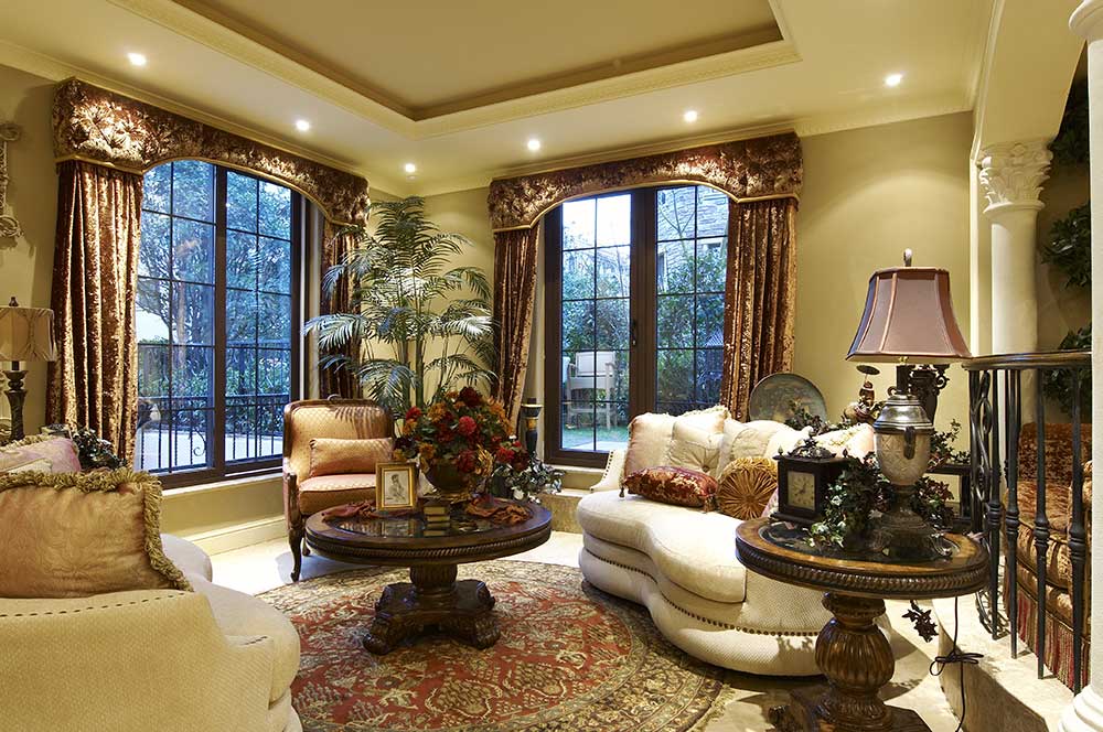 客厅布置在别墅的一层，乳白色沙发搭配红褐色窗帘和桌子，显得高贵华丽，沙发上的沙发垫、桌上摆件都很精致。