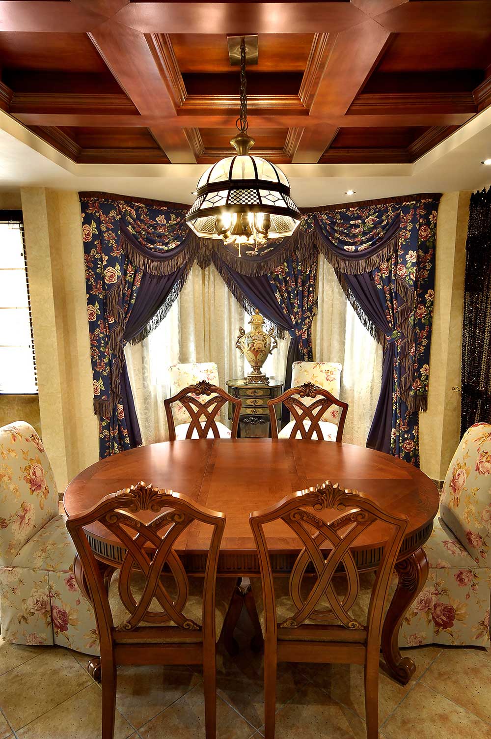 餐厅位于二层，和一层的客厅共用一个吊顶，蓝紫色的绣花窗帘也能够在餐厅被看见。美式风格和田园风格混合在一起。