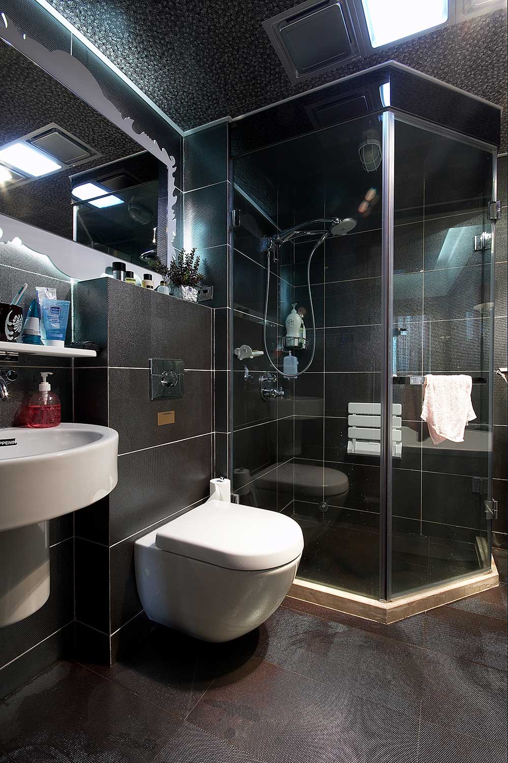卫生间装修具备现代感，黑色墙面砖、吊顶和地砖，整个卫生间空间不易藏污纳垢，玻璃淋浴房让卫生间显得很清爽。