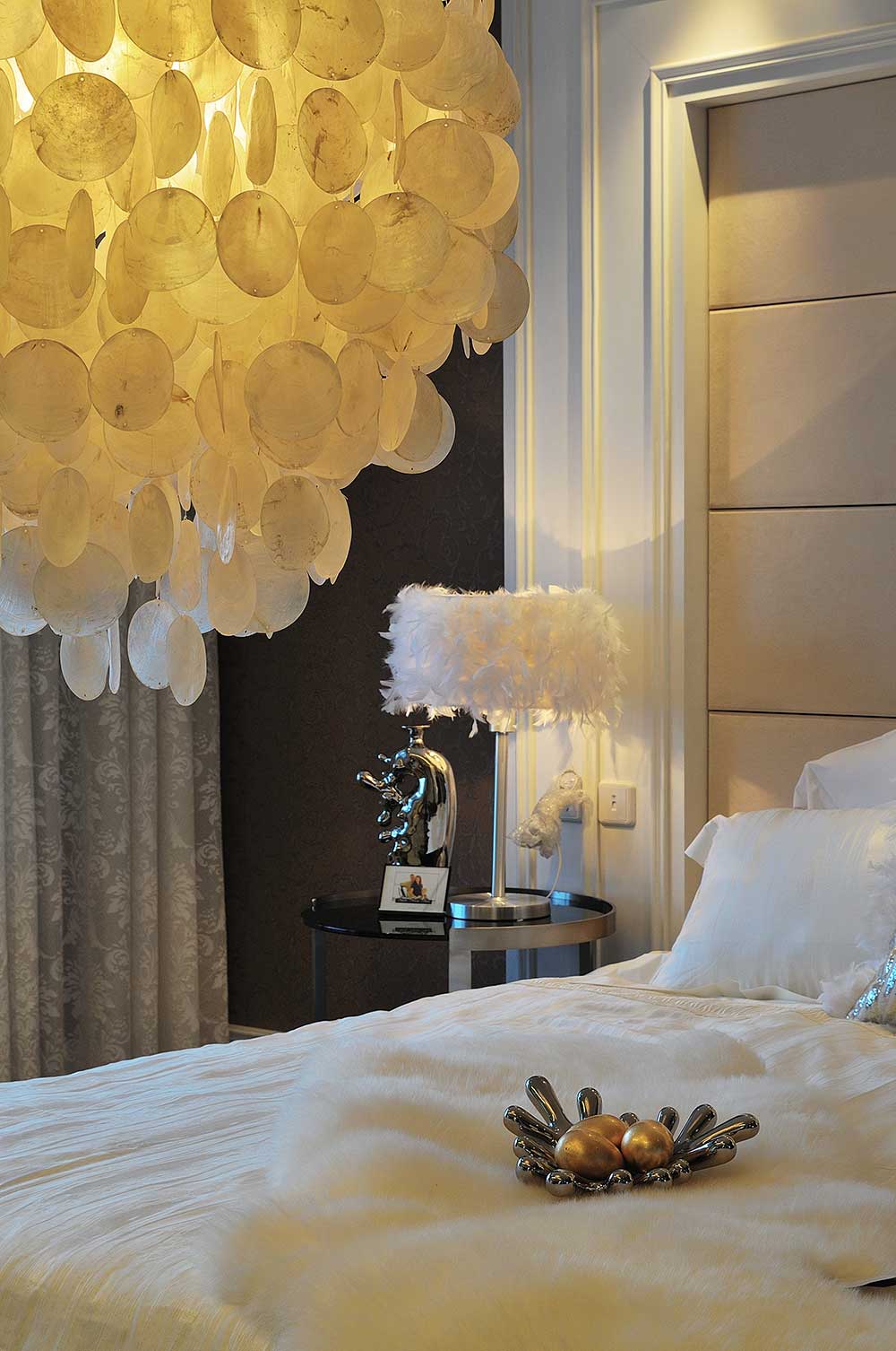 主卧的床上吊灯很华贵，白色羽毛片装饰在灯罩上，微弱的黄光照的整个房间暖暖的，摆件都充满了现代气息。