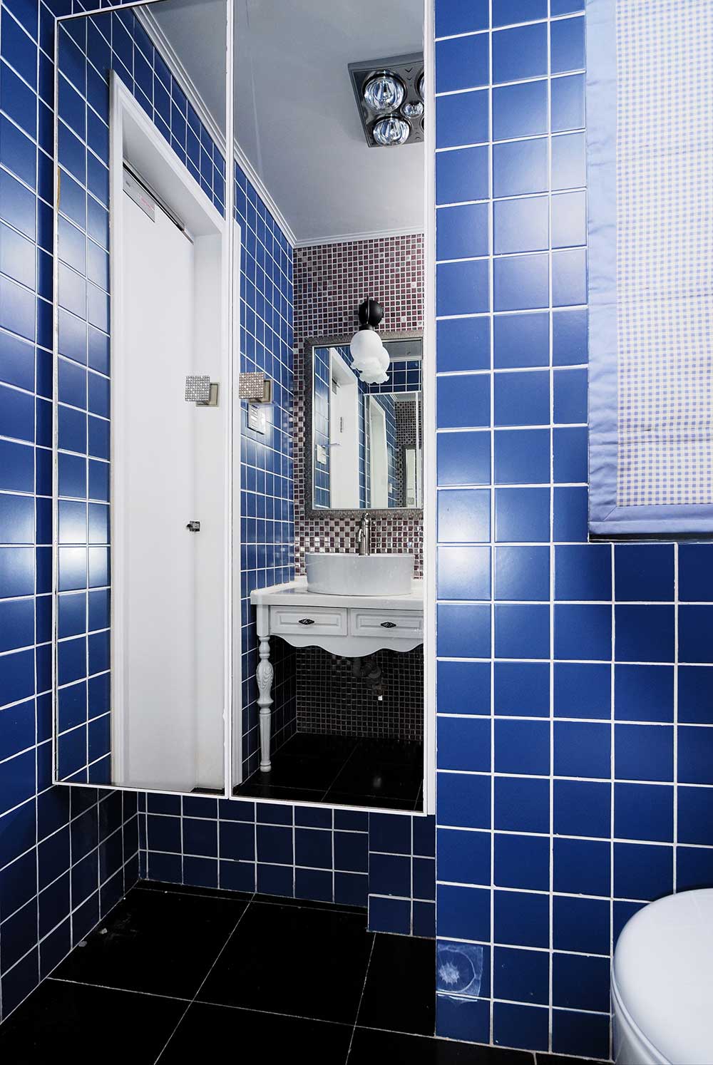 蓝色的瓷砖贴满了整个卫生间，镜面的浴室柜和洗手池的镜子相互反射，复古透亮。