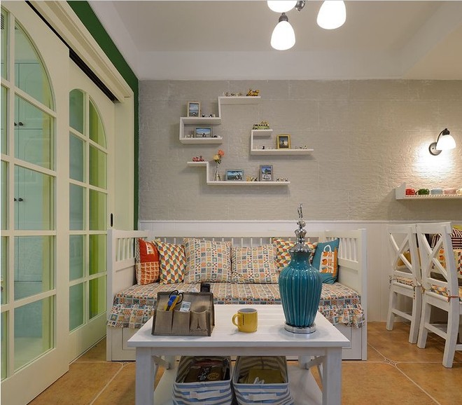 地中海与美式相结合的小户型客厅，沙发采用拼色布艺，五颜六色。背景墙上不规则蜿蜒的装饰架，整齐有序将照片和小饰品收入囊中。