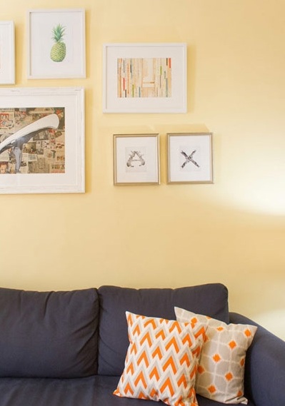 两只带有橙色花纹的抱枕与深色沙发形成对照，同时与橙色茶几相呼应，挑出色彩亮点。沙发背景墙上多幅不同大小的装饰画排列组合，让墙面丰富多彩。