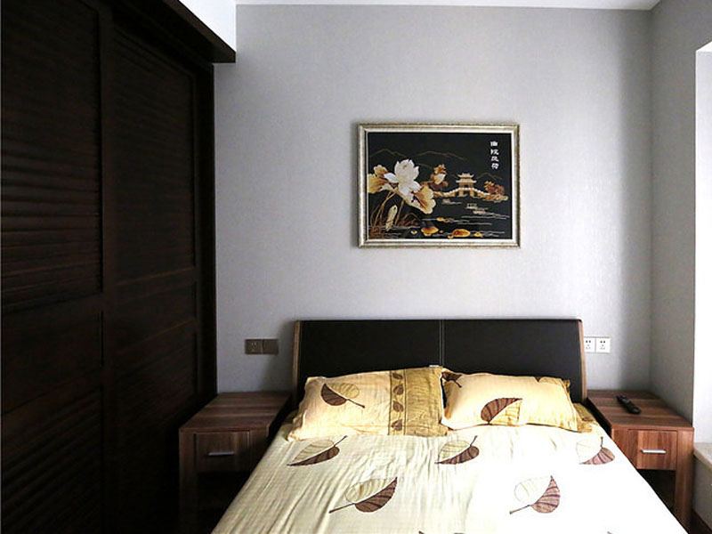床头两边是两个木制的床头柜，正上方挂着一幅配合着衣柜颜色的壁画，整个空间显得对称方正。